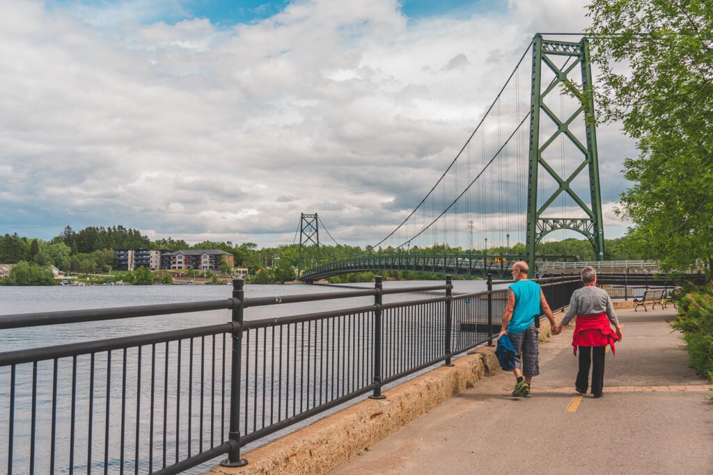 Un couple marche le long de la rivière Saint-Maurice avec le pont de Grand-Mère en arrière-plan